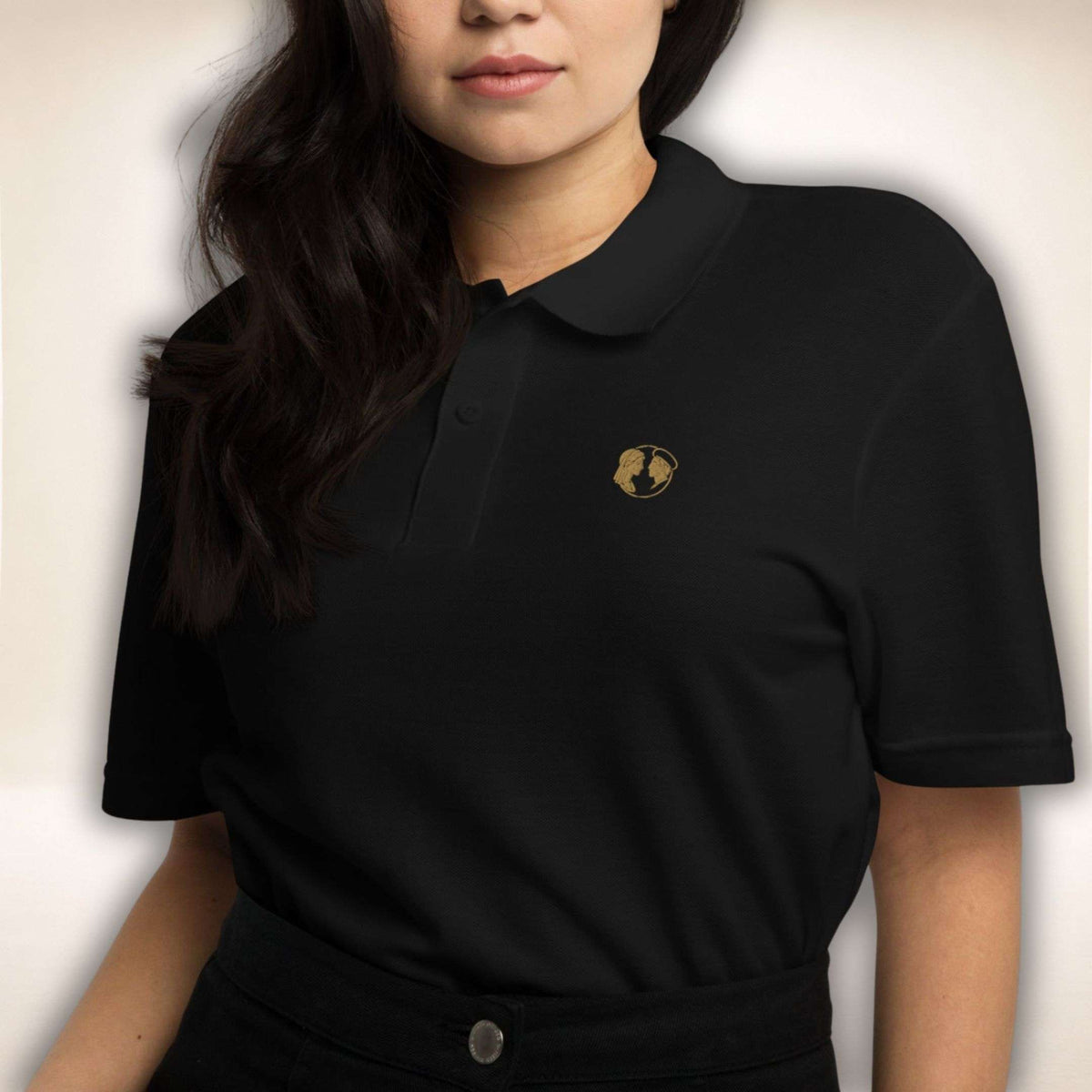 Schwarzes Belgravia Poloshirt mit goldfarbenem Doppelprofil-Logo, von einer Frau getragen